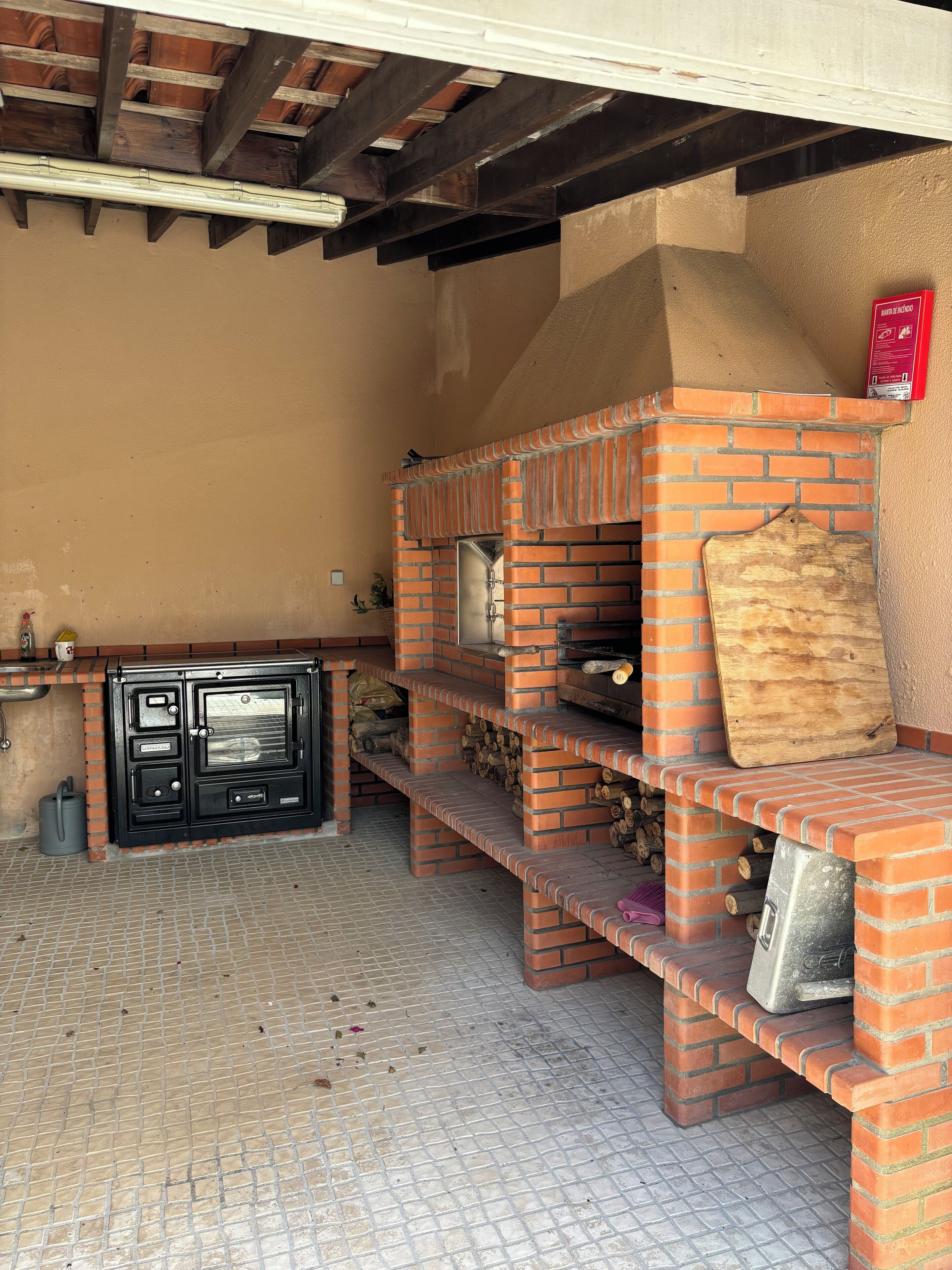 An outdoor brick oven with a wooden cutting board and a fire extinguisher nearby.