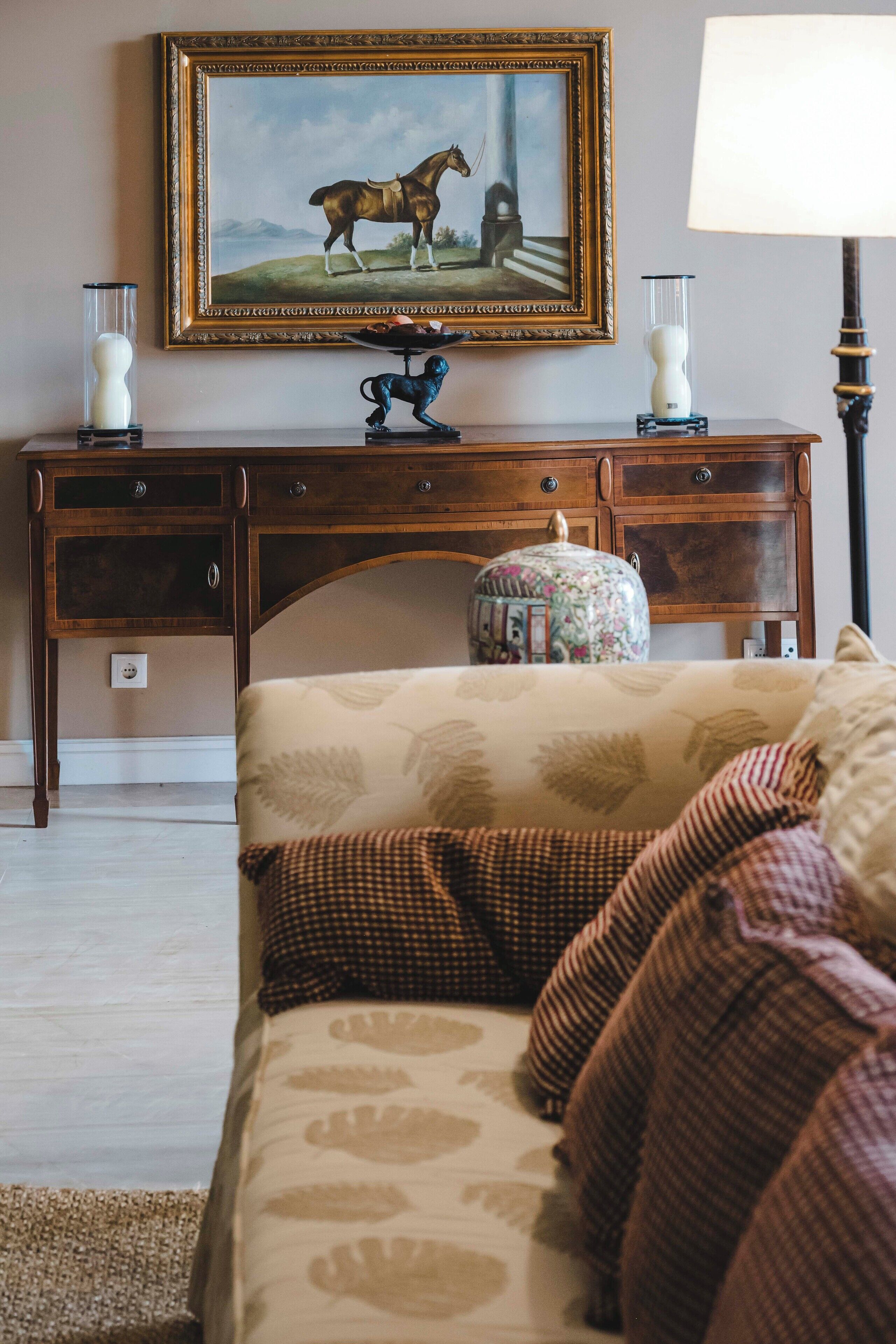 A room with a bed, a wooden desk, a lamp, a vase, and a framed picture on the wall.