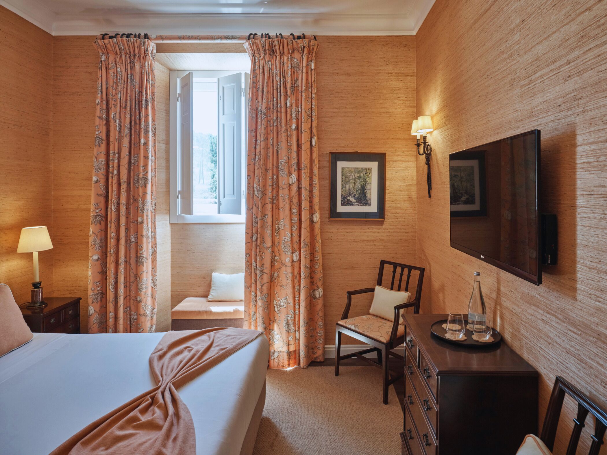 Een hotelkamer met een bed, bureau, stoel, televisie en raam met gordijnen.