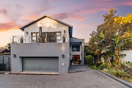 A modern two-story house with a garage, a balcony, and a well-maintained garden.