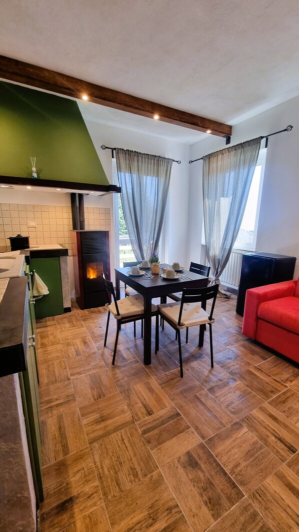 A modern kitchen with a wood-burning stove, a dining area with a table set for four, and a red sofa in a living area. - Bee Freeride Biker house (Magliolo)
