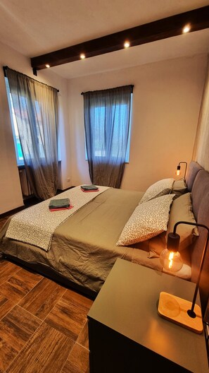 A bedroom with two beds, a bedside table with a lamp, and a window with curtains. - Bee Freeride Biker house (Magliolo)