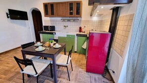 A compact kitchen with a dining table set for four, green and red cabinets, a microwave, and a red refrigerator. - Bee Freeride Biker house (Magliolo)