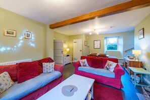 A cozy living room with two red sofas, a white coffee table, and a wooden ceiling beam.