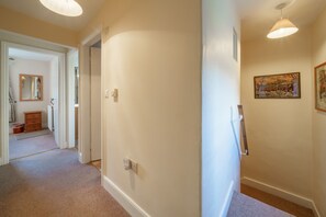 A hallway with beige walls, a wooden dresser, a mirror, and a painting.