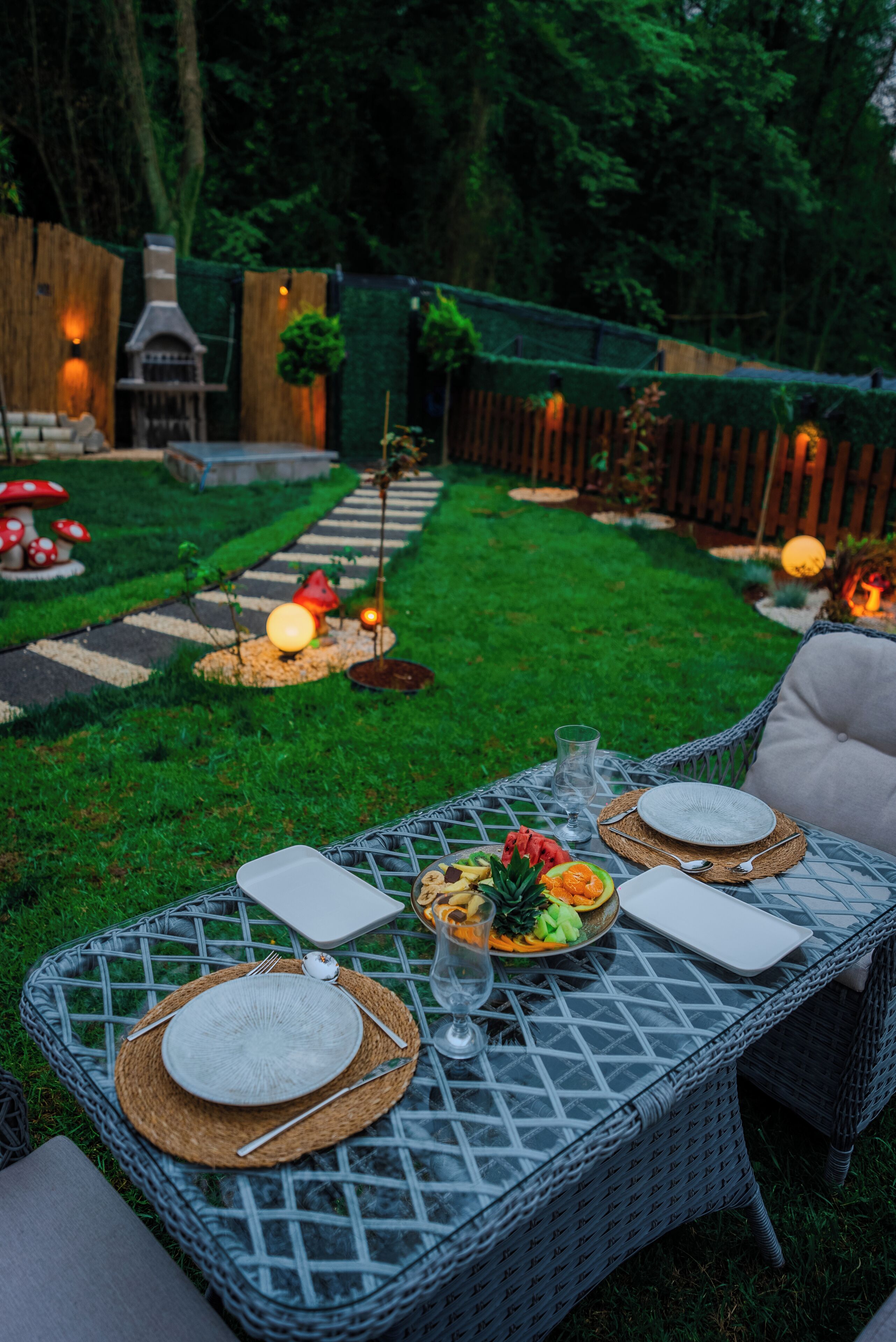 A dining table set outdoors with a wicker table, plates, cutlery, and a glass of water.
