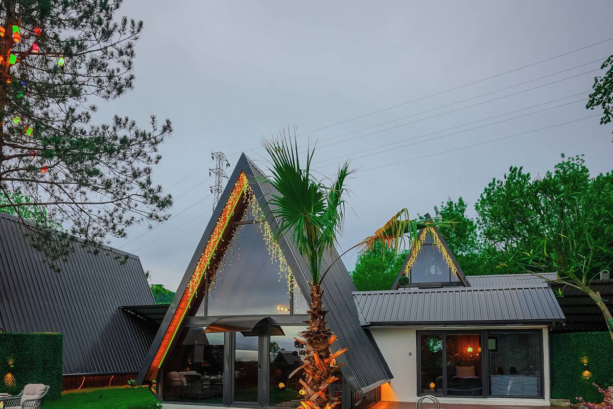 A modern house with a triangular roof, a swimming pool, and a well-maintained lawn.