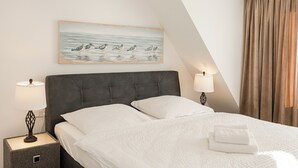 Een net opgemaakt bed met witte lakens en kussens, een donker hoofdbord en een schilderij van vogels aan de muur.