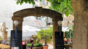 Een terras met stenen bogen, tafels en stoelen. Er staan borden met menu-items en een melding over een waterpartij.