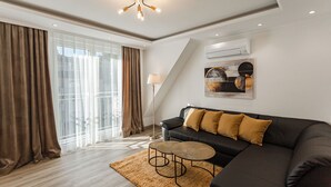 Een moderne woonkamer met een hoekbank, een ronde salontafel en een groot raam met gordijnen.