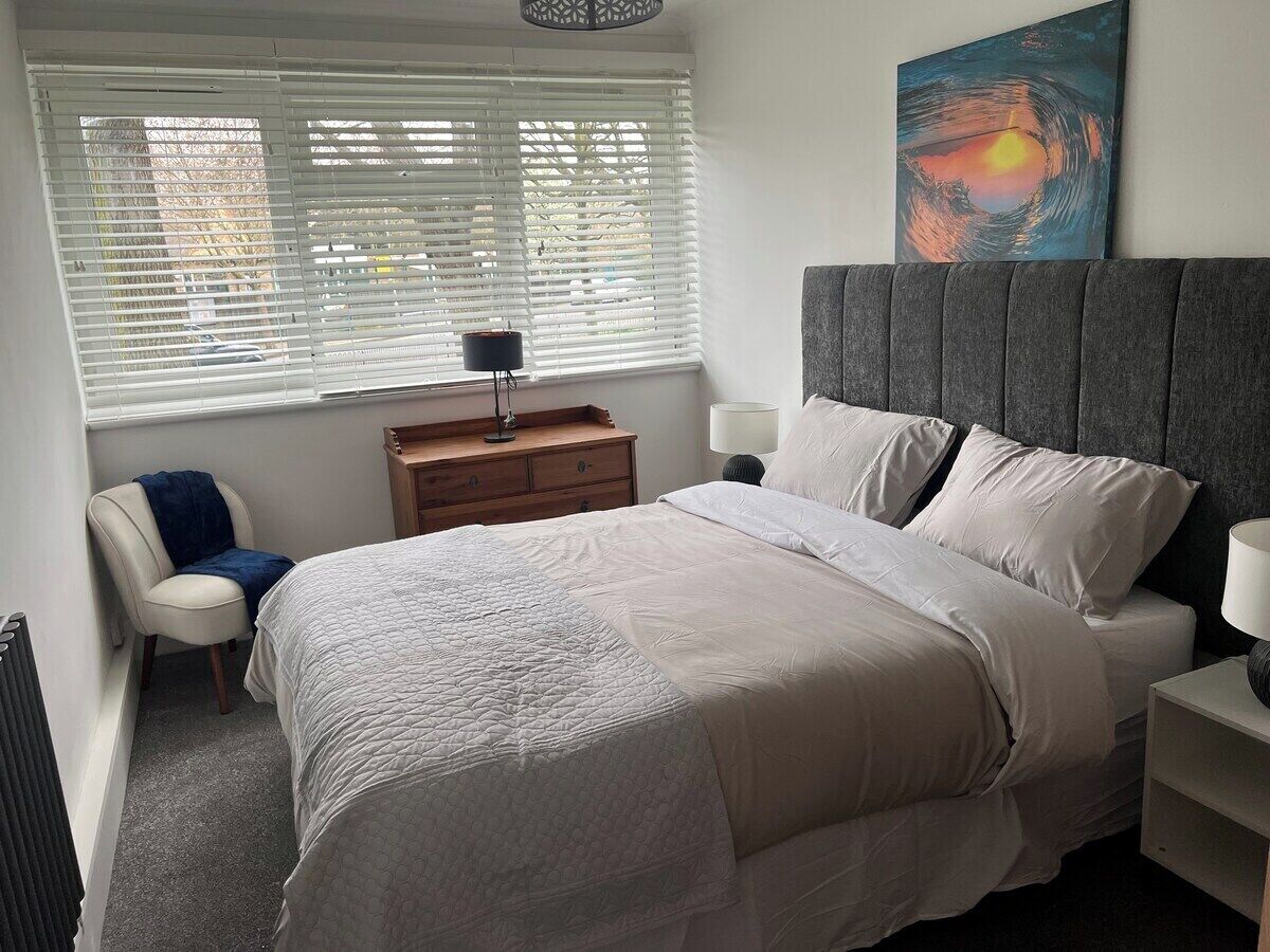 A bedroom with a bed, a chair, a nightstand, a lamp, a dresser, and a painting on the wall.