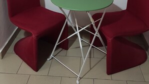 Un tavolino piccolo e rotondo con piano verde, affiancato da due sedie rosse dalla struttura bianca.