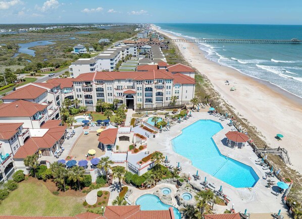 A resort with multiple buildings, a large swimming pool, and a beach.