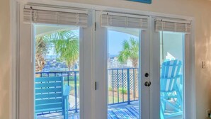 A set of glass doors leading to an outdoor deck with blue chairs and a palm tree. - Villa Capriani 102B - Oceanfront - Pools - Restaurant - Premiere (North Topsail Beach)