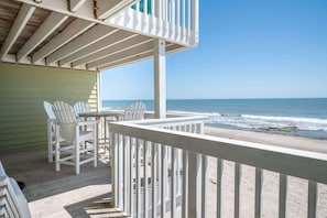 Un balcon donnant sur la plage, avec des chaises et une table blanches, et une vue sur l’océan.