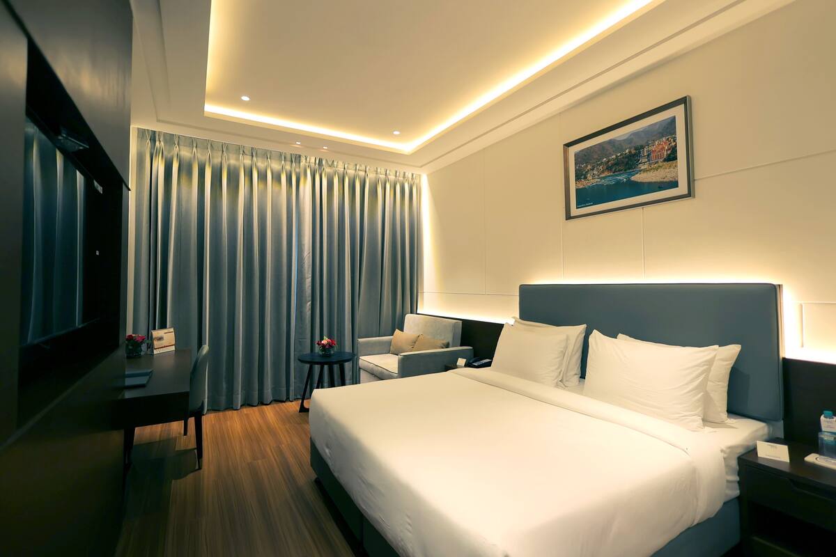 Ein Hotelzimmer mit einem großen Bett, einem Schreibtisch mit Stuhl, einem Fernseher und einem Bild an der Wand.