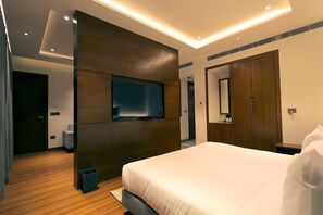 A modern hotel room with a large bed, a flat-screen TV mounted on the wall, a wooden wardrobe, and a small trash bin. - Pride Elite Haridwar (Haridwar)