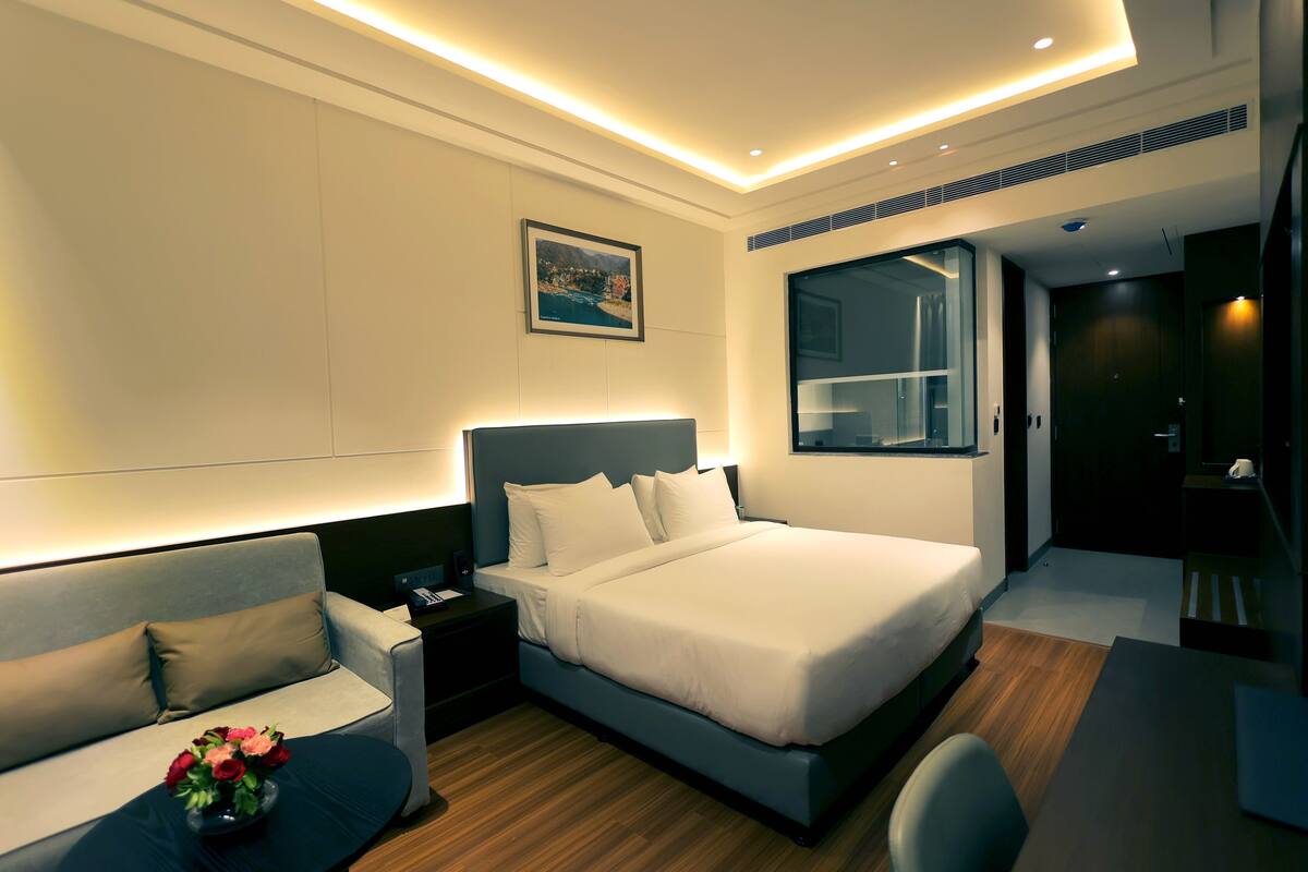 Ein modernes Hotelzimmer mit einem großen Bett, einer Couch, einem Schreibtisch und einem Nachttisch.