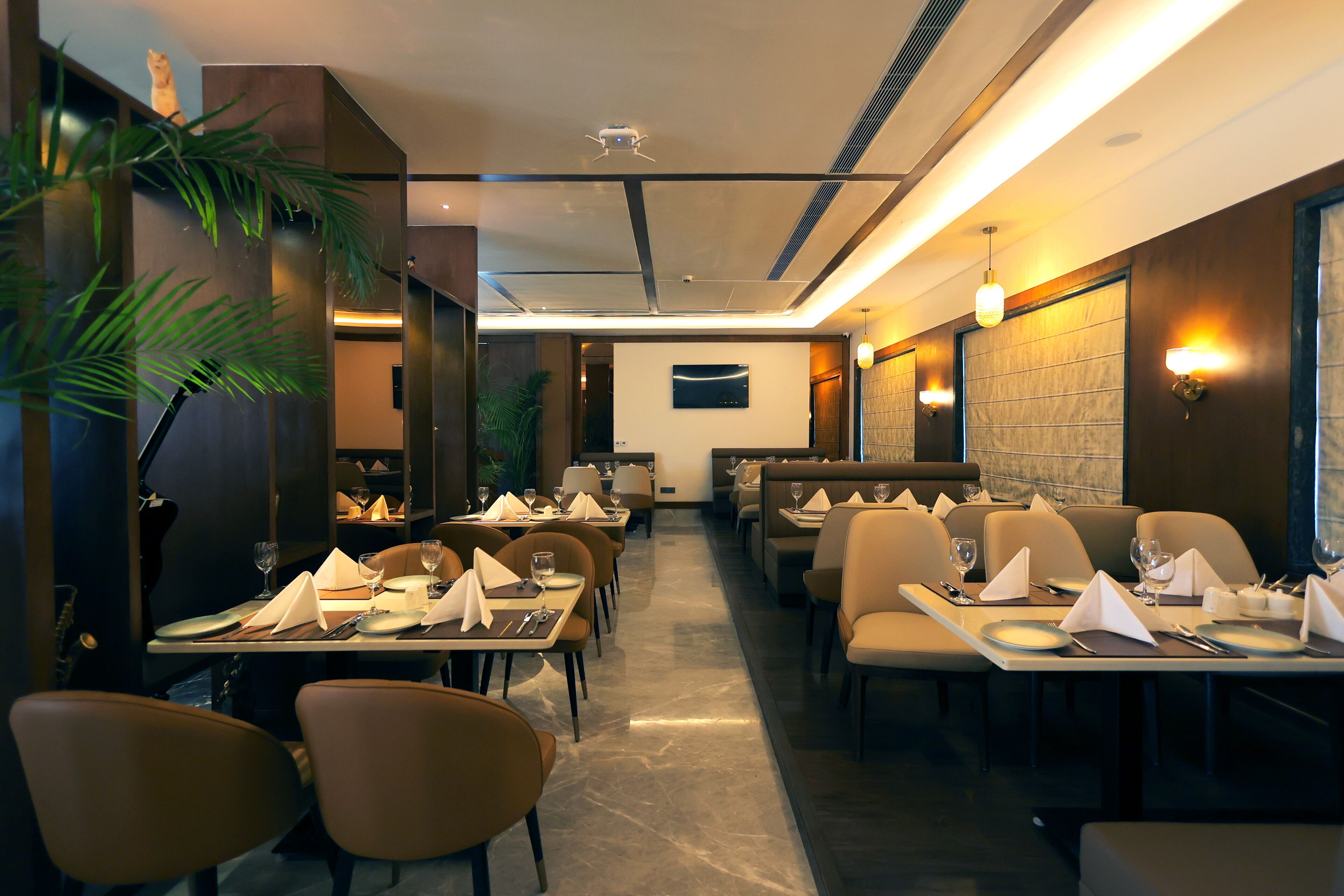 A restaurant with multiple tables and chairs, a flat-screen TV mounted on the wall, and wall-mounted lighting fixtures.