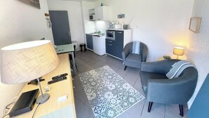 Een compacte woonruimte met een kitchenette, een eethoek en een zithoek met een lamp.