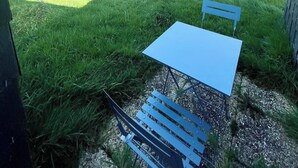 Een terras met een tafel en banken, omringd door een grasveld en een hek.