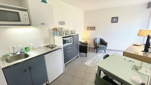 Een kleine keuken met een magnetron, oven en spoelbak. Er is een eethoek met een tafel en stoelen.