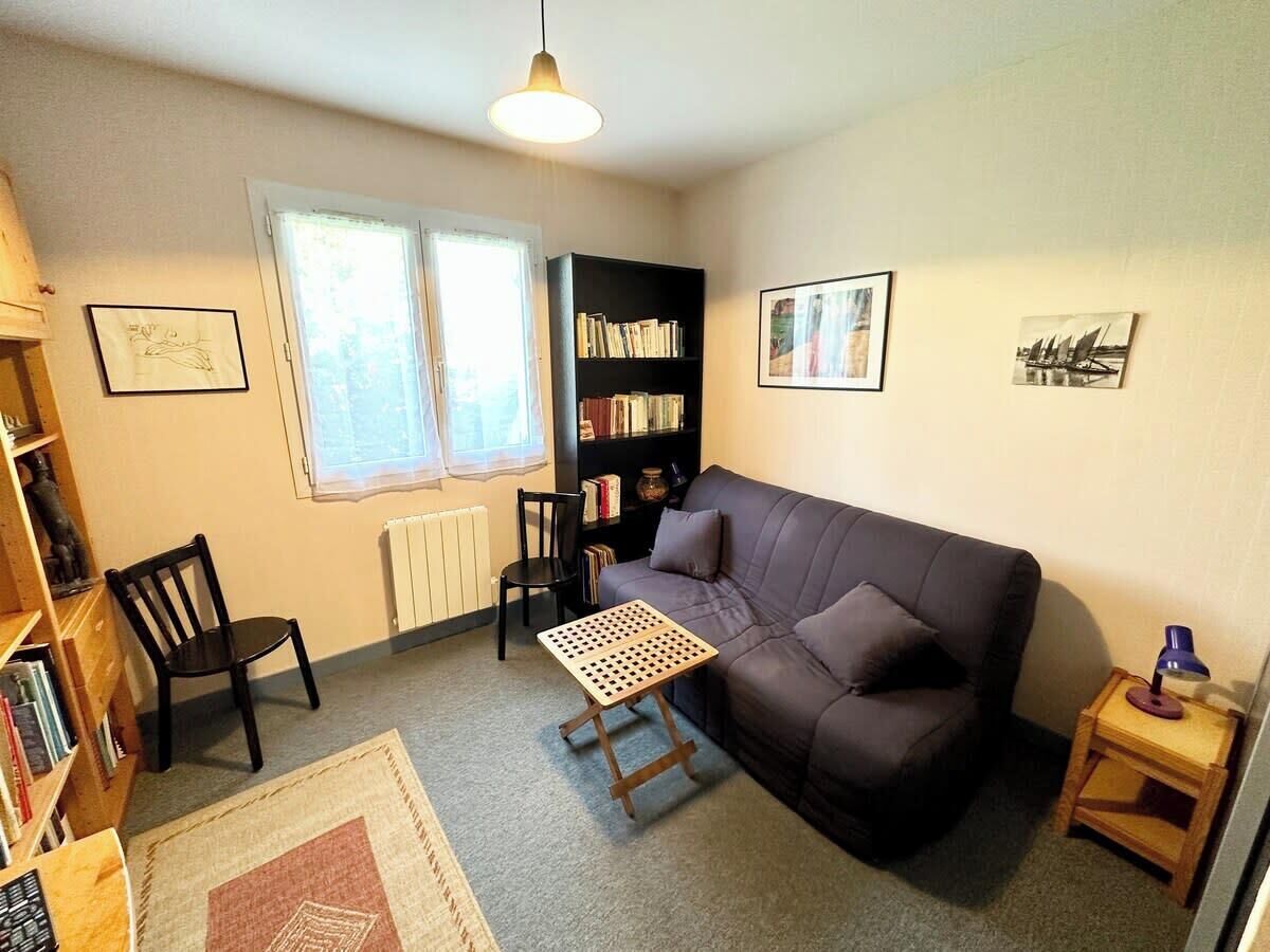 A cozy living room with a dark-colored sofa, a small wooden table, two chairs, a bookshelf, and a radiator.