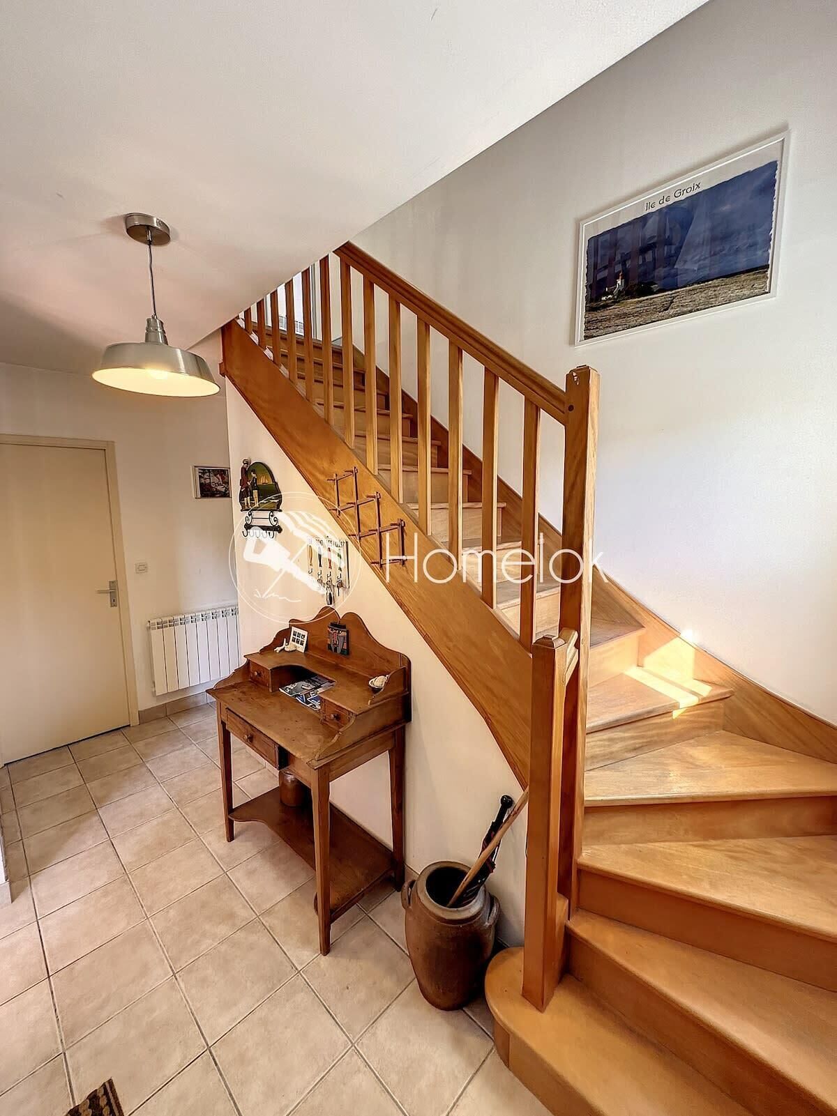 A staircase with wooden railings leading to an upper floor, a hanging light fixture, a small wooden table with items on it, and a radiator on the wall.