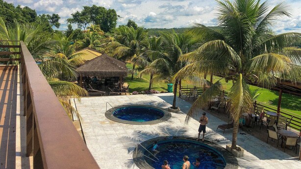 Ein Resort mit Poolbereich, Palmen und einer Struktur mit Reetdach.
