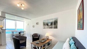 Un salon moderne comprenant un canapé, deux fauteuils, une table basse et une vue sur la mer grâce à de grandes fenêtres.