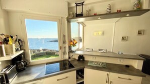 Une cuisine avec vue sur la mer, un fourneau, un évier et des placards.