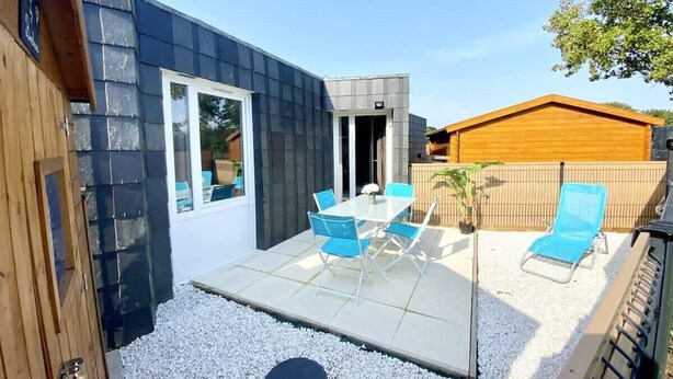 A modern patio with a glass table and blue chairs, surrounded by white gravel and a wooden fence.