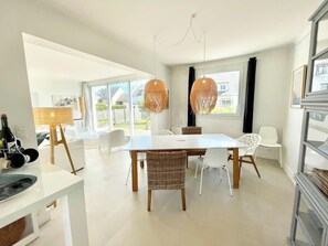 A modern dining area with a white table, wicker chairs, and pendant lights.