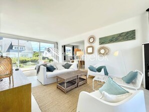 A modern living room with white furniture, a large window, and decorative wall art. - Maison Ultra Coconning Jardin Face aux plages (Ploemeur)
