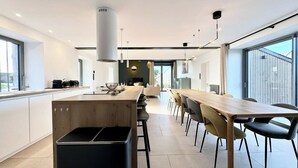 Een moderne keuken met een centraal eiland, een eetgedeelte met een lange tafel, en grote ramen voor veel natuurlijk licht.