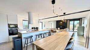 Een moderne keuken met een centraal eiland, barkrukken en een eetgedeelte met een lange tafel.
