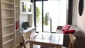 Un salon moderne avec un canapé, une table à manger et un téléviseur. Une porte-fenêtre coulissante donne accès à un balcon.