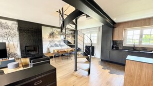 A modern kitchen with a central island, a dining area with a table and chairs, and a spiral staircase leading to an upper level. - Luxury Magnifique Villa d architecte Cocooning (Larmor-Plage)