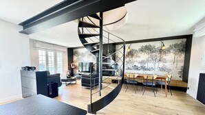 A modern living space with a spiral staircase, a dining area, and a large window with a view of trees. - Luxury Magnifique Villa d architecte Cocooning (Larmor-Plage)