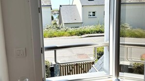 A room with a wooden floor, a glass jar with a doily, and a view of houses through a door.