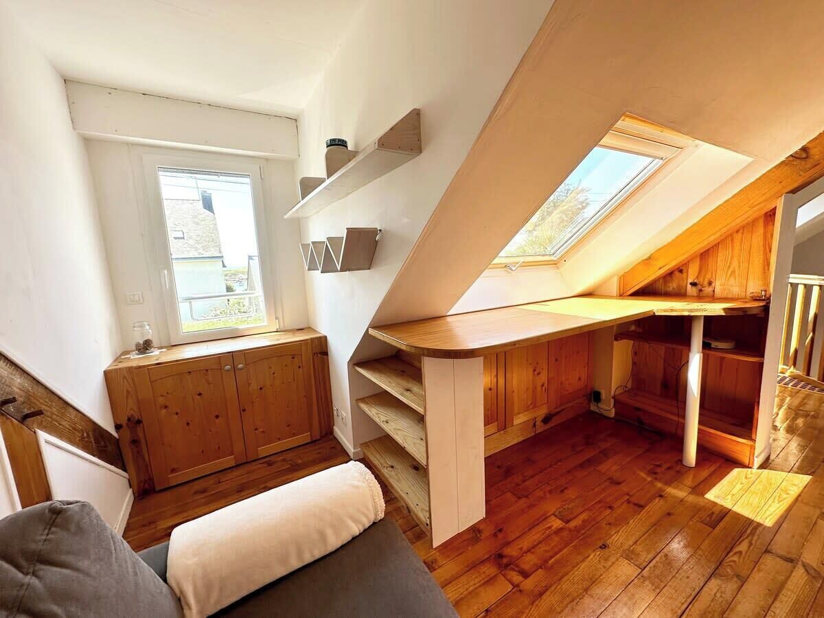 Un dormitorio loft moderno y compacto con techo inclinado, mobiliario de madera y tragaluces.