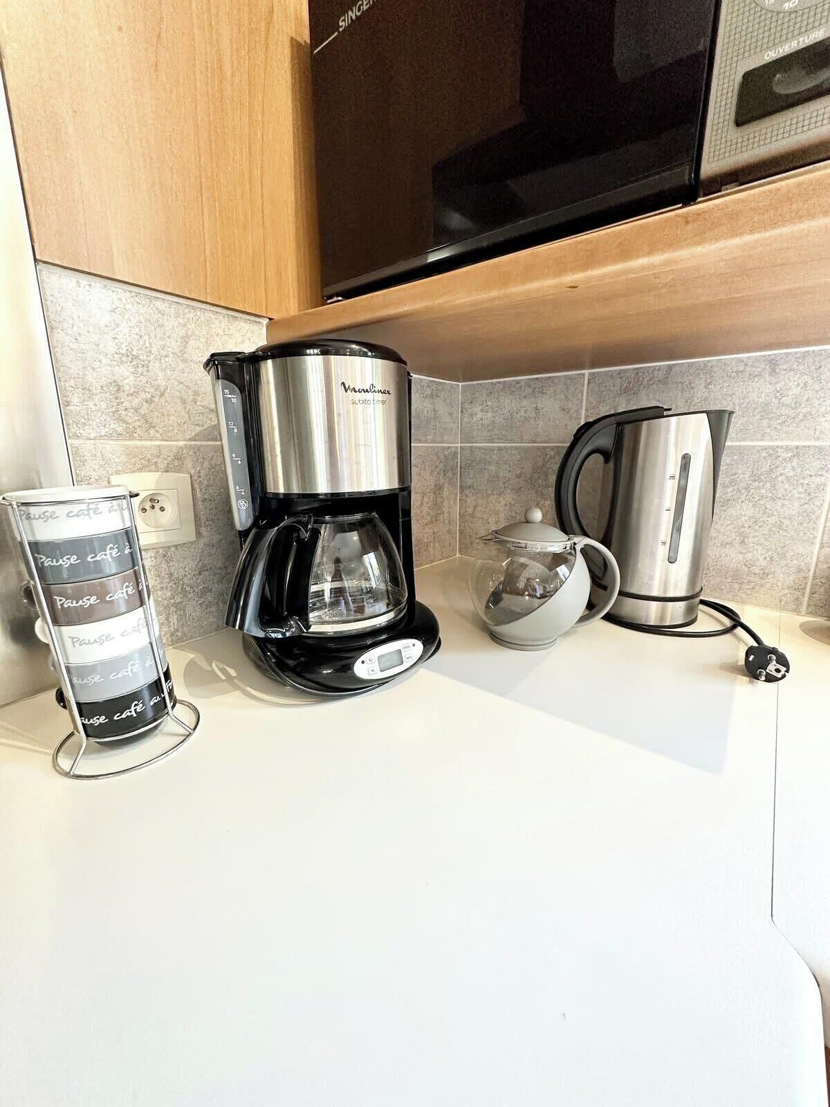 Eine Küchenarbeitsplatte mit einer Kaffeemaschine, einem Wasserkocher und einem Glas Wasser.