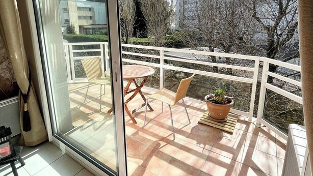 Une pièce dotée d’une porte-fenêtre coulissante donnant sur une terrasse extérieure avec une table et des chaises, une chaise rouge à l’intérieur et une plante en pot sur la terrasse.