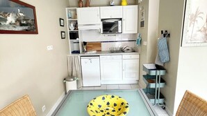 Une cuisine compacte avec des meubles blancs, un four encastré et un petit réfrigérateur.