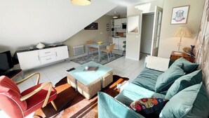 Un salon moderne comprenant un canapé, un fauteuil rouge, une table basse et un coin repas avec une table et des chaises.