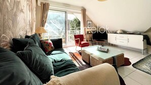 Un salon moderne avec un canapé, un fauteuil rouge et un coin repas comprenant une table et des chaises.