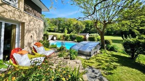 A backyard with a swimming pool, sun loungers, and a covered area.