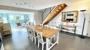 Un comedor amplio con una mesa de madera y sillas blancas, una escalera y vistas al exterior.