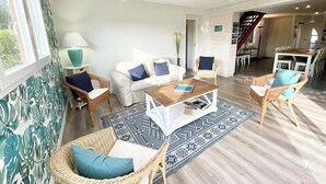 Amplia sala de estar con un sofá blanco, dos sillones de mimbre, una mesa de centro y una alfombra estampada.
