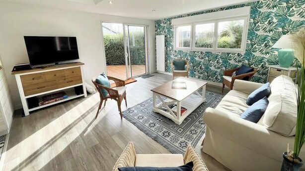 Una sala de estar moderna con televisor, sofá y sillones, una mesa de centro de madera y un tapete estampado.